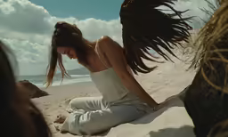 a woman sits on a beach as she looks down at her hair