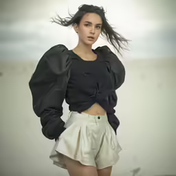 woman standing in white shorts with wind blowing her hair