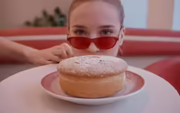 a woman with shades on her face holding a doughnut
