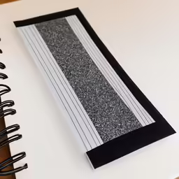 a closeup of the front of a black and white striped notebook with a pen lying beside it