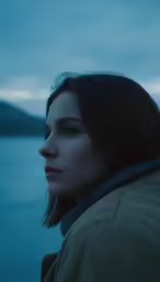a young woman standing near the water with blue tones