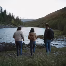 three people are walking along the side of a lake