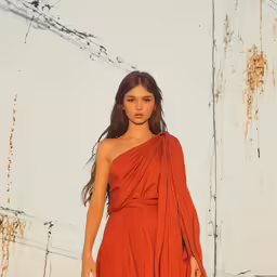 a model walks down the runway in an orange dress