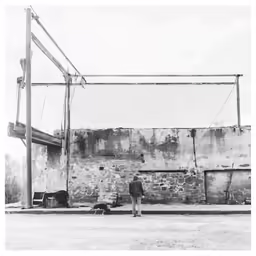a black and white photo of a person with a motorcycle in front of an abandoned building