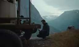 a man sits on top of a hill with his hands clasped looking at his cell phone