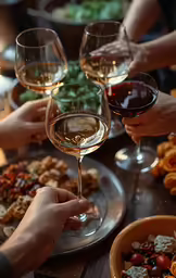 a close up of people holding wine glasses near plates of food