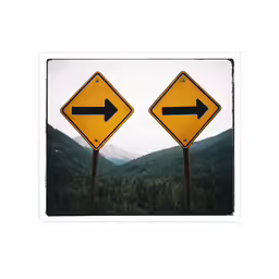 two yellow signs with two black arrows pointing in the same direction