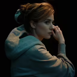 woman in blue coat holding her hand near her face