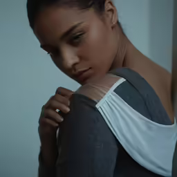 a woman leaning against a wall in a gray top