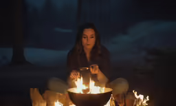 a woman is sitting on the ground near some burning items