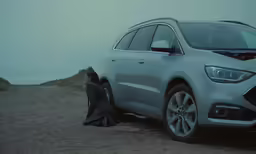 a man kneeling in front of a car on top of a mountain