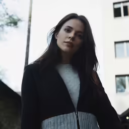 a woman in black and grey standing in front of a tall building