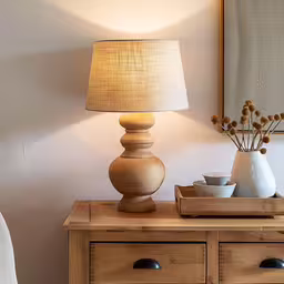 a table that has a wooden shelf next to a lamp,a vase with flowers sitting on top of a wooden table