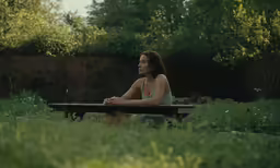 a woman is sitting on a bench in a grass yard