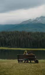 three people sit on a bench facing a body of water