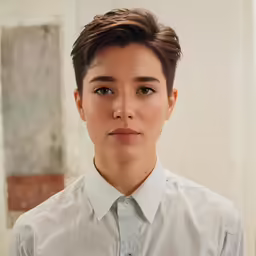 woman with short brown hair and white shirt standing near wall