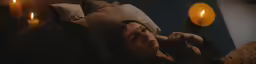 a woman laying in bed on her back with a yellow lit candle next to her