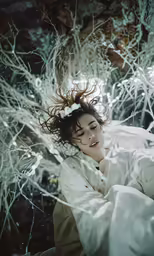 woman in white dress laying on ground under a bunch of tree branches