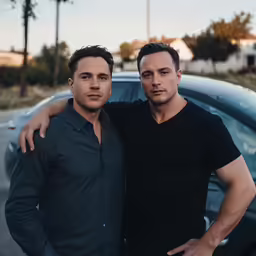 two men standing next to each other near a car