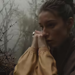 a person standing in the woods with her hands to her chin