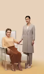 two women in business attire sit on a bench together