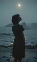 a woman standing on top of a beach under a full moon