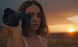 the woman is holding up a camera in the sun set