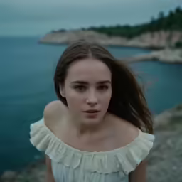 the young woman poses by the water in front of a rock