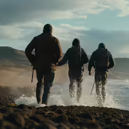 three men are standing with their backs to one another on the shore of the ocean