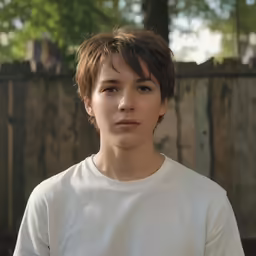 a young man standing next to a fence