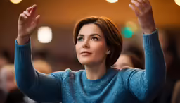 a woman in a blue sweater and her hand raised