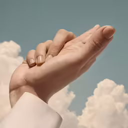 a pair of hands holding each other on a cloud covered sky