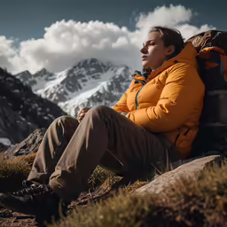 a woman in orange jacket and tan pants on the side of a mountain with a backpack