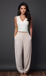 a woman standing in a gray room wearing high rise pants and a white top