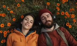 a man and woman are laying on a flowery field with headphones