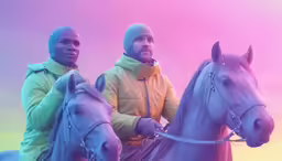 two men dressed in winter gear sitting on top of horses