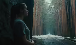 a woman is standing next to the side of a tree - lined road