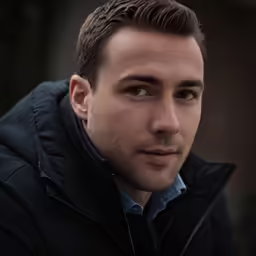 a man looking into the camera, wearing a black jacket