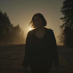 a woman standing in the grass as the sun is setting