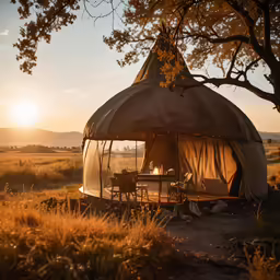 a tent in a field at sunset with a table and chairs