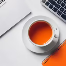 a cup of tea sits next to an open laptop on a white desk