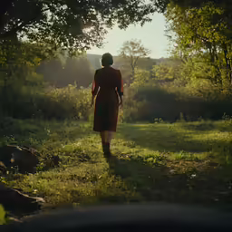 a woman in a red dress walks towards the woods