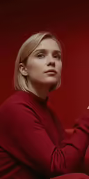 the blonde woman with the red dress sits looking into the distance