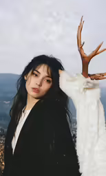 a woman holding onto a white deer head on top of a hill