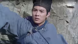 a young man standing by a wall dressed in a traditional clothing,man in blue clothes standing next to rock face