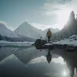 man in yellow jacket by mountain and lake with snow