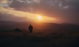 a man standing on top of a lush green hill under a cloudy sky