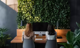 two young women sitting in office chairs and one using a computer