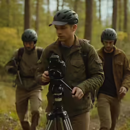 two men walking across a forest while holding onto a camera
