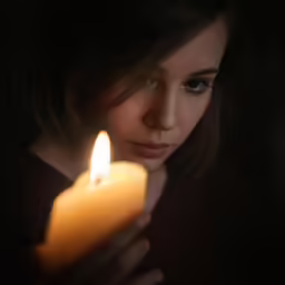 a woman is looking at her reflection as she holds the candle in the dark